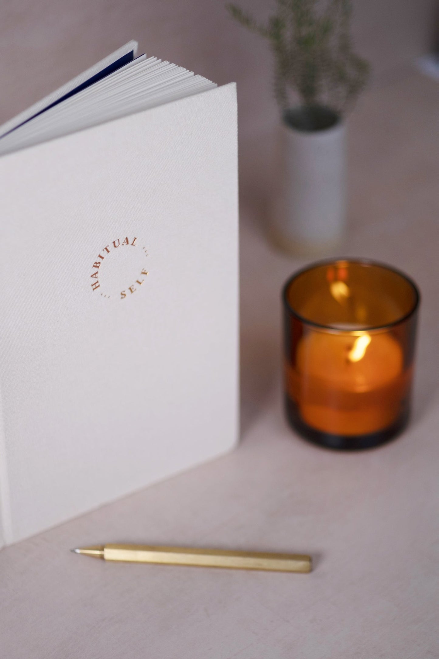 The Archely's Habitual Self Journal beside a candle, styled for a peaceful journaling moment
